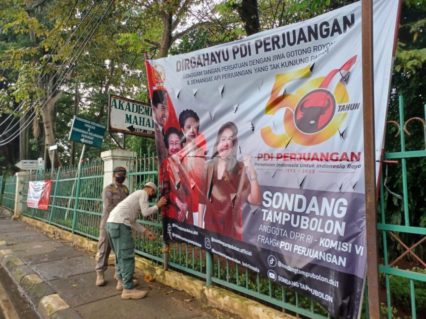 Empat aparat personel Satpol PP Kelurahan Susukan, Kecamatan Ciracas, Jakarta Timur, menurunkan spanduk partai di sepanjang Jalan Raya Bogor, Rabu (1/3). Foto: Joesvicar Iqbal/ipol.id