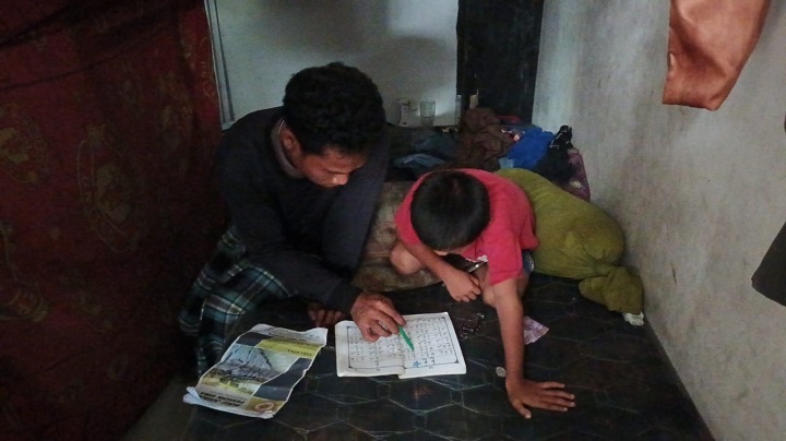 Abdullah mengajarkan anaknya yakni Alka, 8, untuk belajar membaca, berhitung dan mengaji di sebuah ruangan tempat keduanya menumpang di pos keamanan cafe tempatnya bekerja di kawasan Kalisari, Jakarta Timur, Jumat (14/4). Foto: Ist