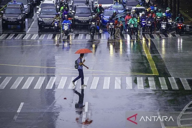 Seorang pekerja menggunakan payung untuk menghindari hujan saat menyeberangi jalan di kawasan Jalan MH Thamrin, Jakarta. (ANTARA)