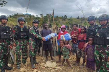 Prajurit Satgas 330 memberikan bantuan terpal untuk atap honai yang sedang dibangun oleh Martin, warga Intan Jaya, Papua. Foto: Ist