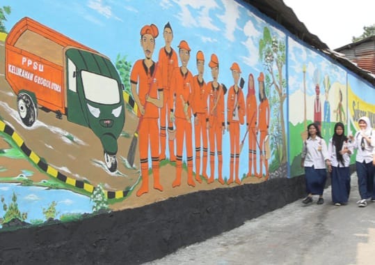 Para pelajar SMP merasa nyaman berjalan kaki melintasi tembok yang dilukis mural oleh petugas penanganan prasarana dan sarana umum (PPSU) di Jalan Inspeksi Kali Grogol, RT 001/RW 005, Kelurahan Grogol Utara, Kecamatan Kebayoran Lama, Jakarta Selatan, Selasa (12/12).