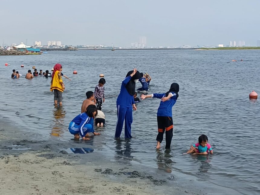 Para pengunjung, keluarga dan anak-anak menikmati bermain pasir putih di bibir pantai Ancol Taman Impian Jakarta. Foto: Dok/ipol.id