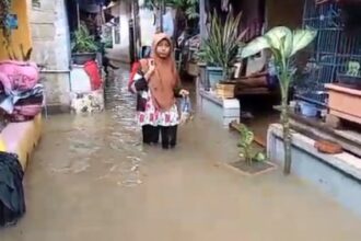 Seorang Ibu warga di Jalan Cipinang Bali, Cipinang Muara, Jatinegara, Jakarta Timur, Rabu (31/1), berjalan menerabas banjir untuk melakukan aktivitas keseharian. Foto: Joesvicar Iqbal/ipol.id
