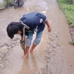Sulit mencari air bersih, seorang peziarah di TPU Mangunjaya Muhammad Nabil terpaksa mencuci kakinya di kubangan air di jalan. Foto: Yudha Krastawan/ipol.id