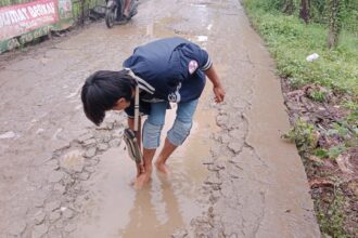 Sulit mencari air bersih, seorang peziarah di TPU Mangunjaya Muhammad Nabil terpaksa mencuci kakinya di kubangan air di jalan. Foto: Yudha Krastawan/ipol.id