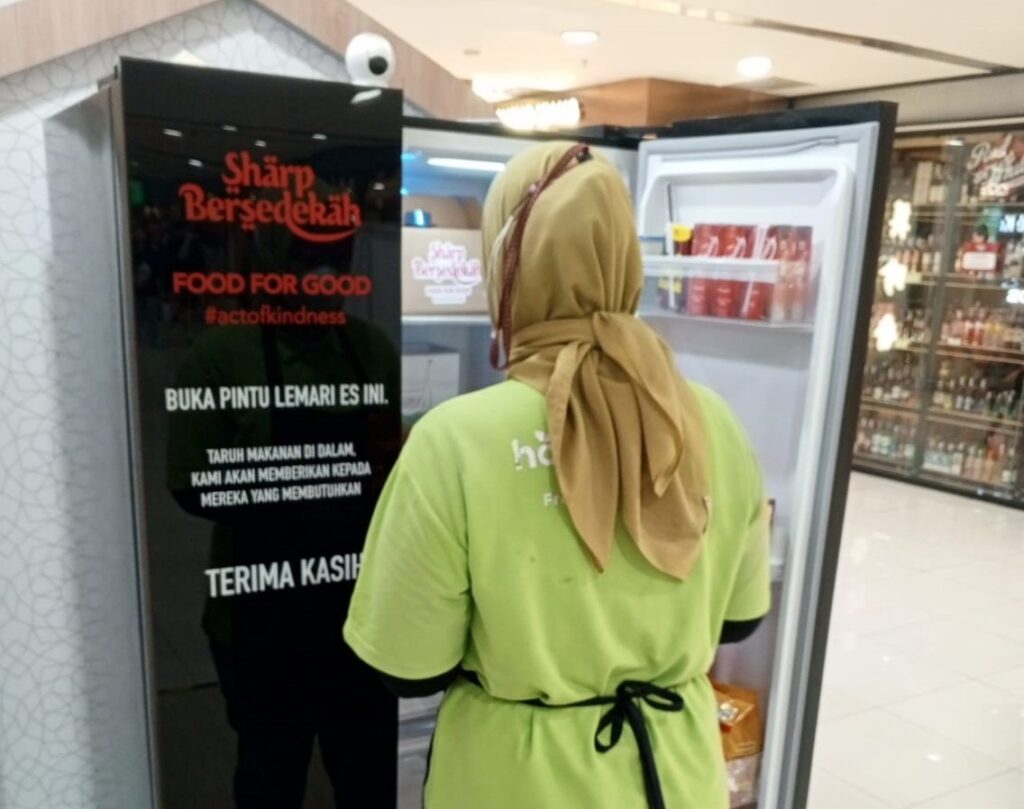 Salah satu pengunjung memasukan donasi makanan ke dalam lemari es pada program Sharp Bersedekah