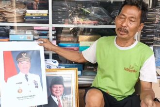 Pedagang foto frame, Kasbari menunjukkan bingkai foto Teguh Setyabudi yang resmi baru dilantik sebagai Penjabat (Pj) Gubernur DKI Jakarta di tokonya di kawasan Jatinegara, Jakarta Timur, Senin (21/10/2024). Foto: Joesvicar Iqbal/ipol.id