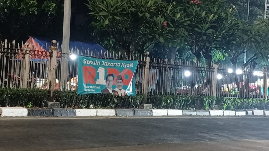 Salah satu alat peraga kampanye salah satu paslon pada Pilkada Jakarta 2024 terbentang di pagar pembatas jalan di Jalan Raya Bogor, Kramat Jati, Jakarta Timur, belum lama ini. Foto: Joesvicar Iqbal/ipol.id