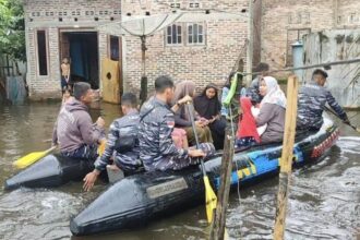 Prajurit Pangkalan TNI AL (Lanal) Tanjung Balai Asahan membantu warga menggunakan perahu karet menuju TPS dari rumahnya yang terendam banjir. Foto: Puspen TNI