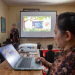 Guru Pasraman yang ada di Desa Ngadiwono, Tosari, Pasuruan, Jawa Timur, sedang mengajar menggunakan media laptop dan proyektor yang baru saja didapat dari pemberian hibah NeutraDC melalui program CSR, Two Hands Hub NeutraDC. Foto: Telkom Indonesia