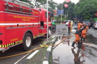 Tiga personel Suku Dinas Penanggulangan Kebakaran dan Penyelamatan Jakarta Timur melakukan penyemprotan bekas tumpahan oli solar di Jalan TMII Pintu 1, Kelurahan Ceger, Kecamatan Cipayung, pada Kamis (29/5/2025). Foto: Ist