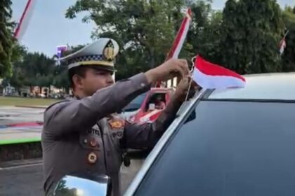 Kasat Lantas Polres Kudus, AKP Royke N Darean dan jajaran Satlantas Polres Kudus membagikan dan memasangkan ratusan bendera merah putih ke sejumlah unit kendaraan pengendara roda dua dan roda empat di sekitar kantor Bupati Kudus, Kamis (7/8/2025). Foto: Ist