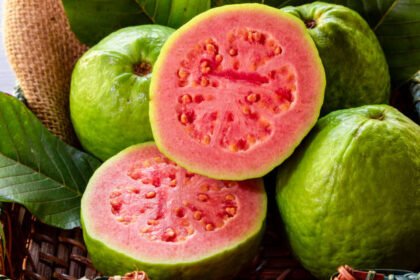 Ilustrasi, jambu biji merah dipotong menjadi dua, di latar belakang beberapa jambu biji dan daun hijau. Foto: Istcok @Murilo Gualda