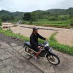 Pengendara motor melintas dengan latar belakang kondisi jembatan gantung Cimanisan yang roboh diterjang banjir bandang di Desa Toblong, Kecamatan Peundeuy, Kabupaten Garut, Jawa Barat, Sabtu (15/11/2025). Foto: Ist