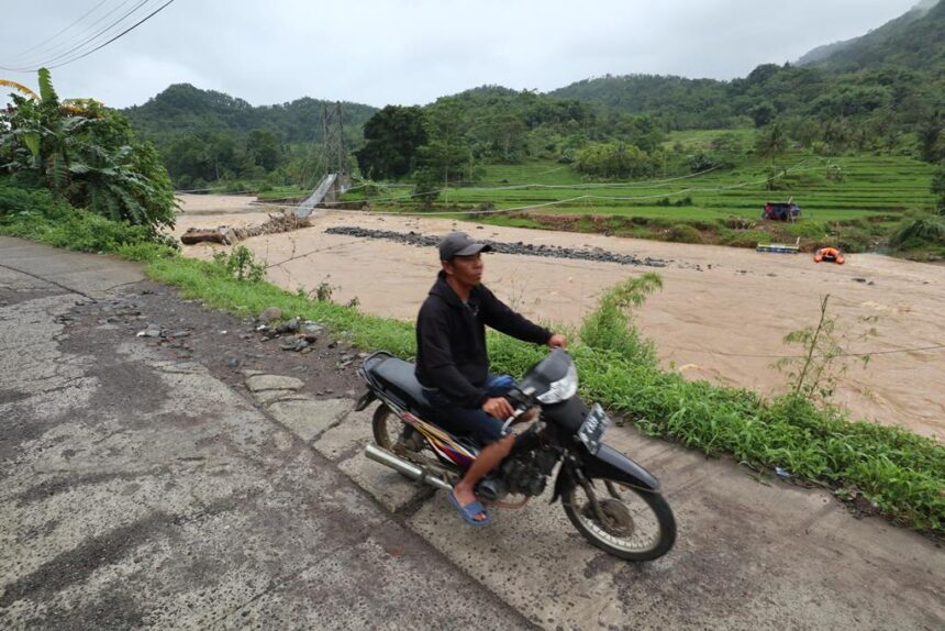 Pengendara motor melintas dengan latar belakang kondisi jembatan gantung Cimanisan yang roboh diterjang banjir bandang di Desa Toblong, Kecamatan Peundeuy, Kabupaten Garut, Jawa Barat, Sabtu (15/11/2025). Foto: Ist