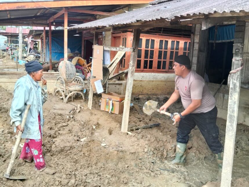 Personel Posko 1 Batalyon C Pelopor Sat Brimob Polda Sumatera Utara membantu membersihkan lumpur tebal yang menutupi pekarangan rumah warga di Desa Aek Ngadol, Kecamatan Batang Toru, Jumat (12/12/2025). Foto: Ist