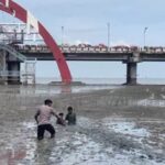 Personel Dit Polairud Polda Jawa Timur, Bharada Nevan saat melakukan evakuasi dua anak terjebak di lumpur di kawasan wisata Pantai Kenjeran, Surabaya, Jawa Timur, Sabtu (3/1/2026). Foto: Ist
