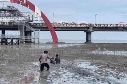 Personel Dit Polairud Polda Jawa Timur, Bharada Nevan saat melakukan evakuasi dua anak terjebak di lumpur di kawasan wisata Pantai Kenjeran, Surabaya, Jawa Timur, Sabtu (3/1/2026). Foto: Ist