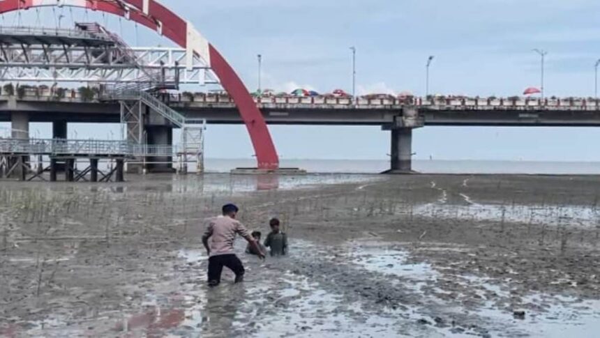 Personel Dit Polairud Polda Jawa Timur, Bharada Nevan saat melakukan evakuasi dua anak terjebak di lumpur di kawasan wisata Pantai Kenjeran, Surabaya, Jawa Timur, Sabtu (3/1/2026). Foto: Ist