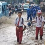 Suasana tiga siswa Sekolah Dasar (SD) berjalan kaki menerabas genangan di Jalan Raya Bogor, Kramat Jati, Jakarta Timur, mengarah traffick light Pusat Grosir Cililitan, Senin (12/1/2026) siang. Foto: Joesvicar Iqbal/ipol.id