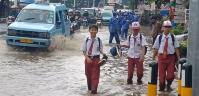 Suasana tiga siswa Sekolah Dasar (SD) berjalan kaki menerabas genangan di Jalan Raya Bogor, Kramat Jati, Jakarta Timur, mengarah traffick light Pusat Grosir Cililitan, Senin (12/1/2026) siang. Foto: Joesvicar Iqbal/ipol.id